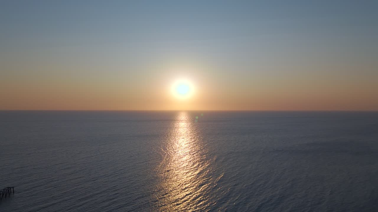 Drone glides laterally from north to south while facing the setting sun. The reflection dances across the ocean’s surface, capturing motion, light, and color in a graceful sunset journey.