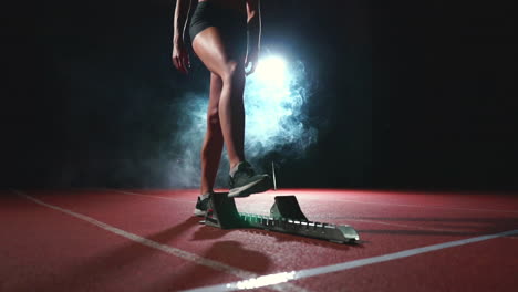 young woman athlete in black shorts and a t-shirt is preparing to start in the race for 100 meters on the treadmill near the start line