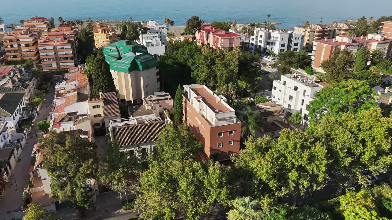 Aerial view of coastal city buildings surrounded by green trees in sunlight