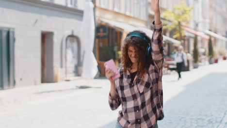happy young woman in wireless headphones listening favorite energetic music in urban city street