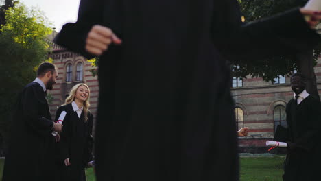 happy multi ethnical graduates tossing caps and running in the park near university on a sunny graduation day