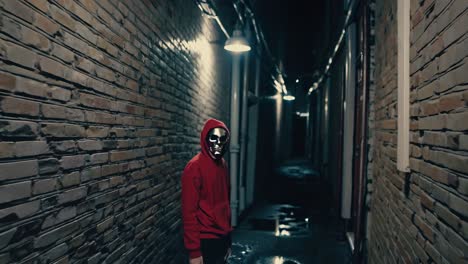 person in red hoodie and mask walking in a dark alley at night