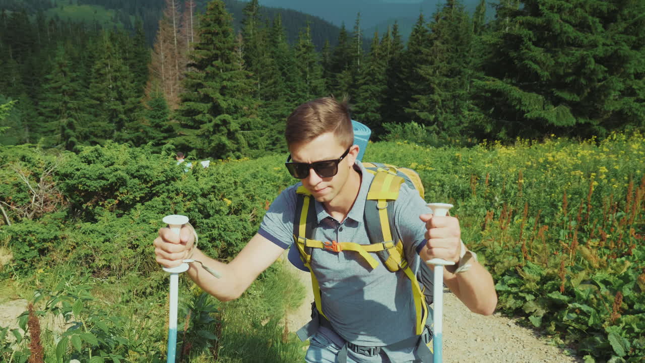 молодой турист поднимается в гору, используя треккинговые палки, на фоне живописного ск