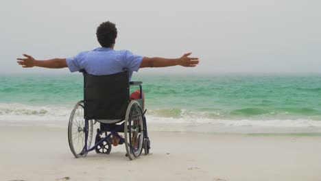 vista trasera de un hombre afroamericano sentado con los brazos extendidos en silla de ruedas con los brazos extendidos