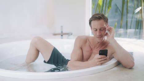 young man reads messages on smartphone in modern bathtub
