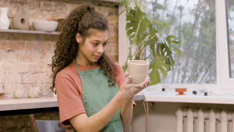 clerk woman looking at a ceramic piece that she has modeled on the potter wheel