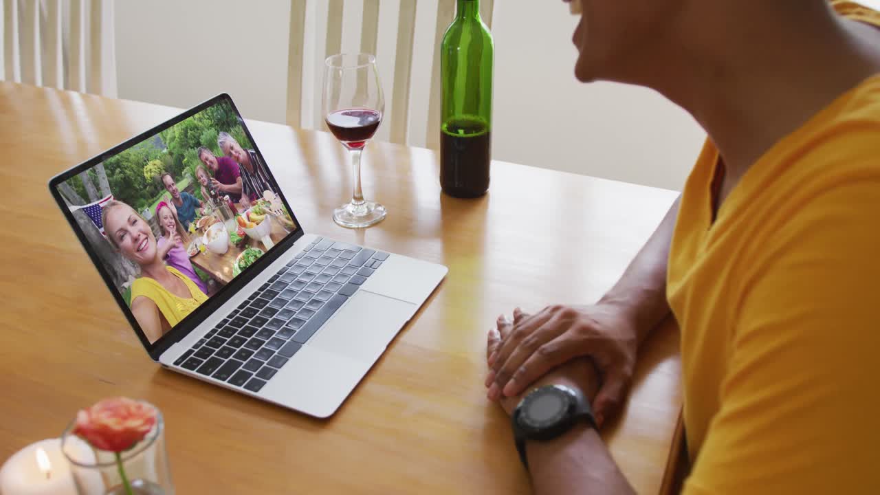 Mixed race man sitting at table using laptop making video call with family