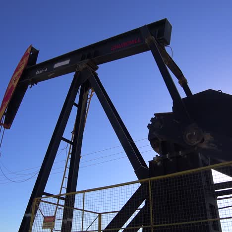 Low-angle-of-oil-derrick-pumping-against-blue-sky