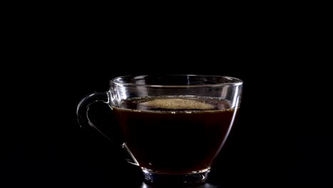 coffee is poured into a glass cup against a black background, highlighting the rich color and texture of the liquid