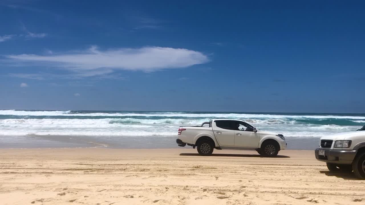 Looking out across the beach towards the azure ocean on a stunning summer's day, as 4x4 four wheel drive vehicles drives past in both directions, on North Stradbroke Island's Main Beach
