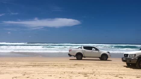 looking out across the beach towards the azure ocean on a stunning summer's day, as 4x4 four wheel drive vehicles drives past in both directions, on north stradbroke island's main beach