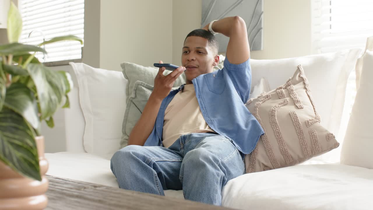 Tapping smartphone for voice note at home, African American man leaning on couch recording response
