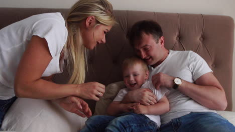 Loving-parents-play-with-their-son-on-the-bed-laughing-and-smiling-in-the-bedroom