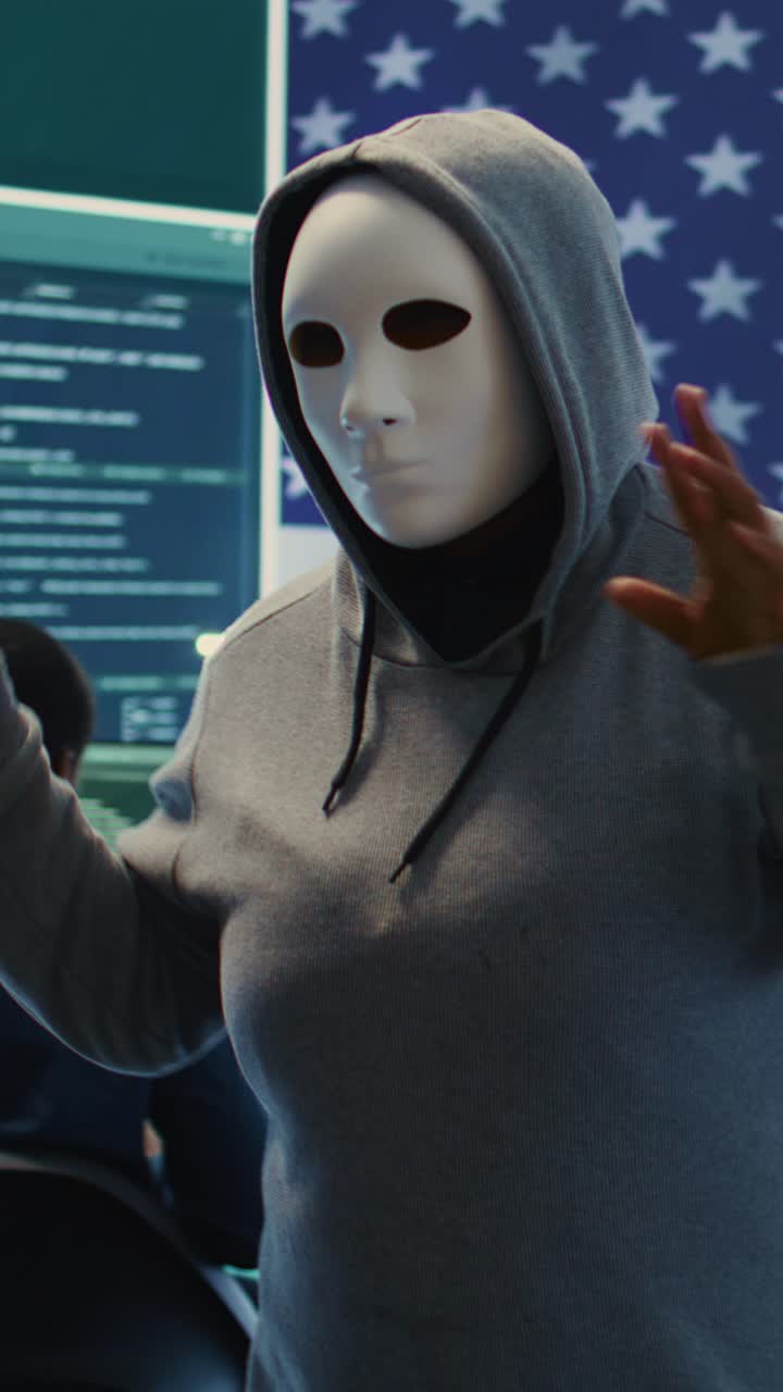 Masked Hacker Gesturing in Front of American Flag and Computer Screens