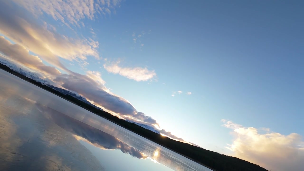 A tranquil view of Laguna La Zeta with smooth water reflecting clouds and distant snow-capped mountains near Esquel, Argentina at golden hour.