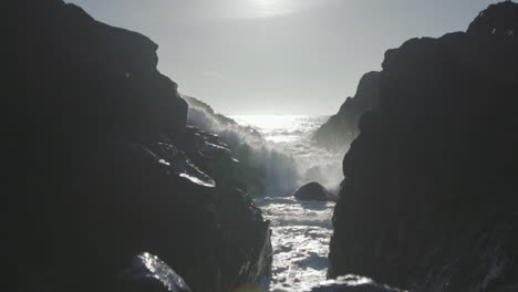 primer plano de ángulo bajo en cámara lenta de una ola oceánica rompiendo rocas y fluyendo hacia la cámara