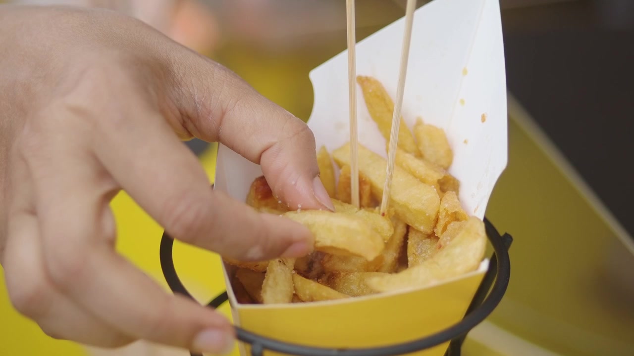 Una mano alcanzando una patata frita crujiente de una caja de papel