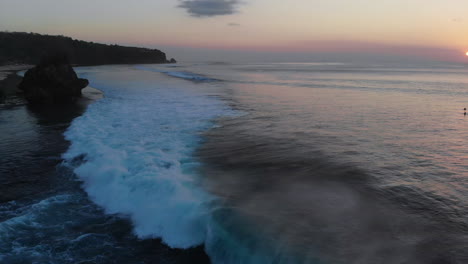 a unique shot of a 5-6 foot wave breaking close the shore, nature, open ocean, incredible sunset and surfers int he background