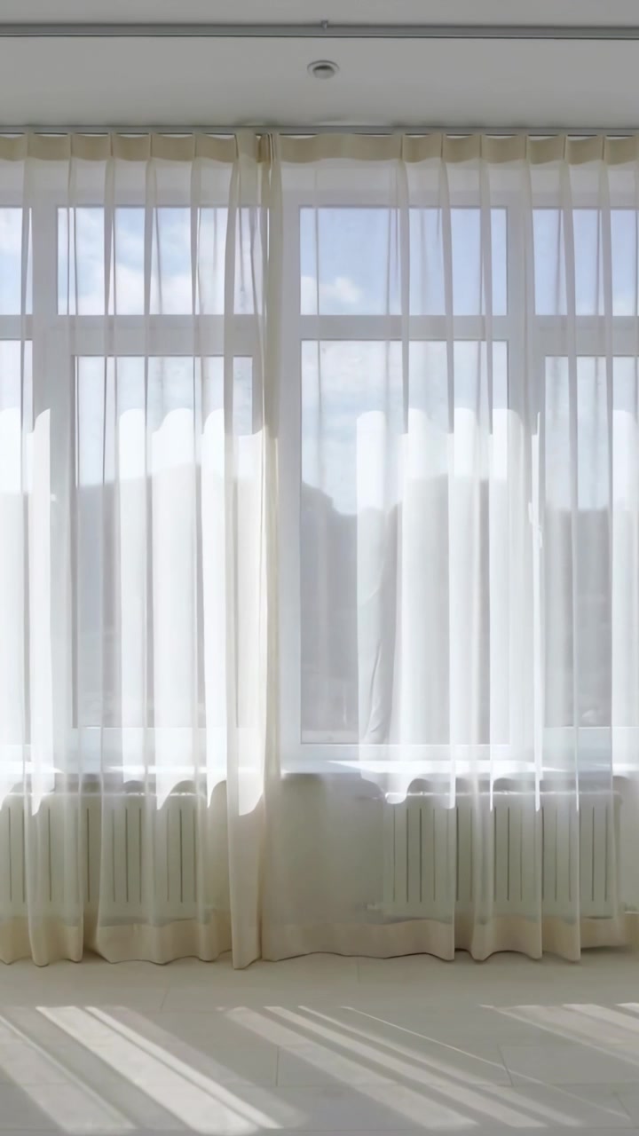 Vídeo vertical: Cortinas transparentes balançando na janela da brisa movendo a luz no chão claro do estúdio