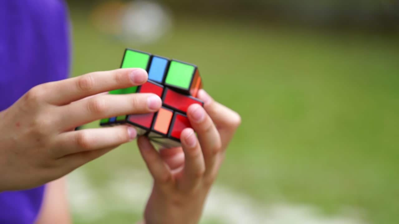 Close-up of rubik's cube in boy's hands. Boy is holding rubik cube and solving puzzle of one of the world's best-selling toys on blur green background.