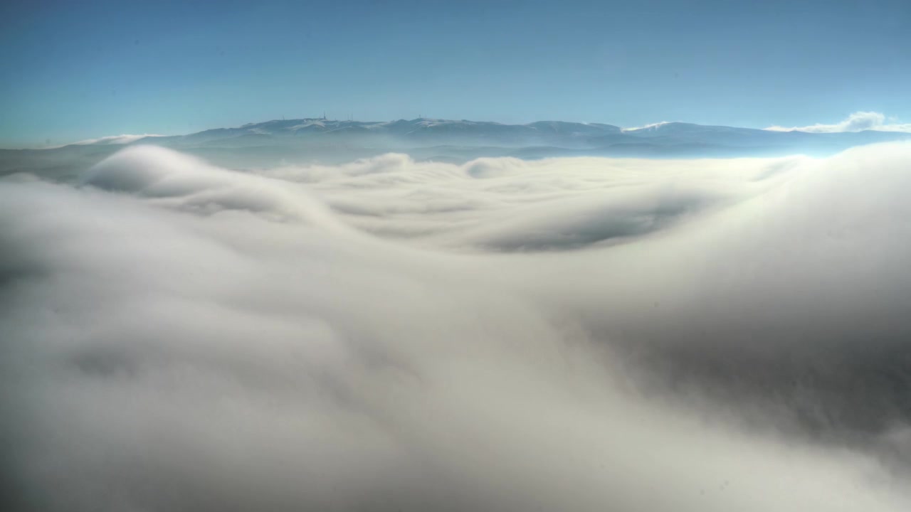 Aerial View of Thick Clouds Rolling Over Mountain Landscape