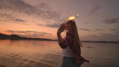 Hermosa-Mujer-Sonriendo-En-Verano-Con-Bengalas-Bailando-Girando-A-Cámara-Lenta-En-La-Playa-Por-La-Noche.