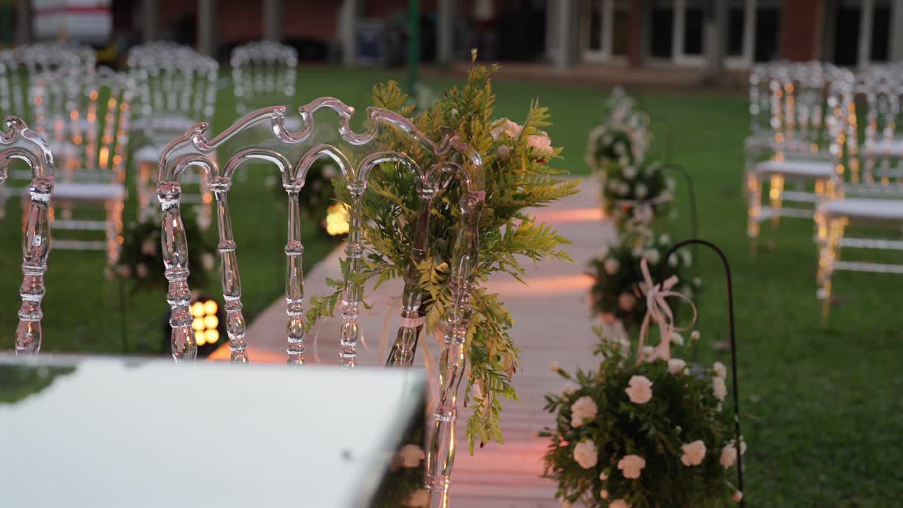 Un corridoio nuziale in giardino splendidamente decorato presenta sedie trasparenti e luci soffuse durante il crepuscolo.