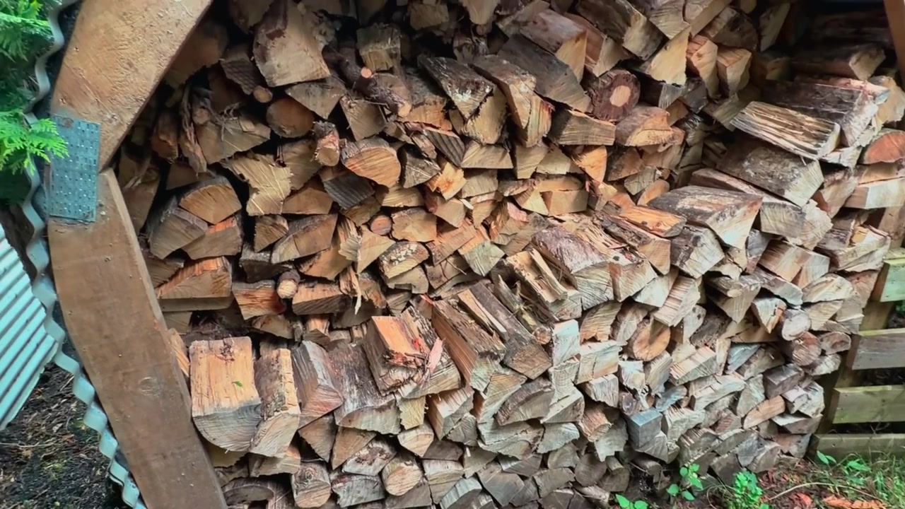 A neatly stacked pile of firewood sits in a peaceful rural setting in New Zealand. Natural timber prepared for heating, showcasing a traditional countryside lifestyle.