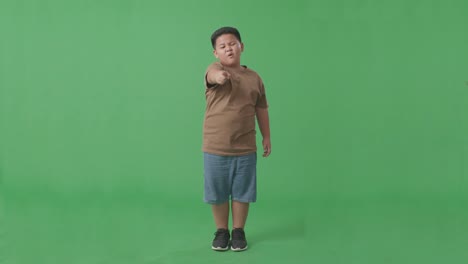 cuerpo lleno de chico asiático enojado regañando mientras estaba de pie en la pantalla verde en el estudio