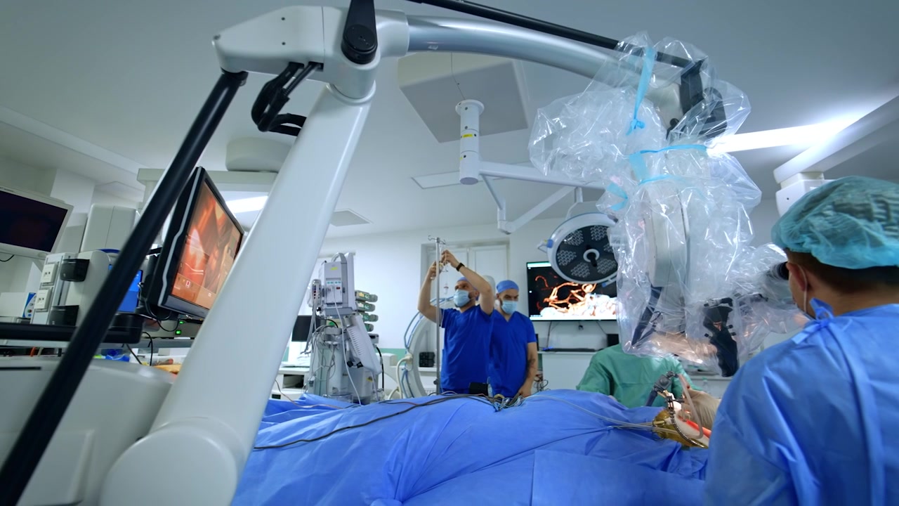 Sala de cirugía moderna y bien equipada con personal médico trabajando dentro. Cirujanos que miran por el microscopio operan a un paciente. Anestesiólogos revisan el goteo intravenoso y los signos vitales en los monitores