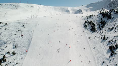 high drone shot tilting up over a busy ski slope in andorra, rising toward a snow-covered mountain summit.