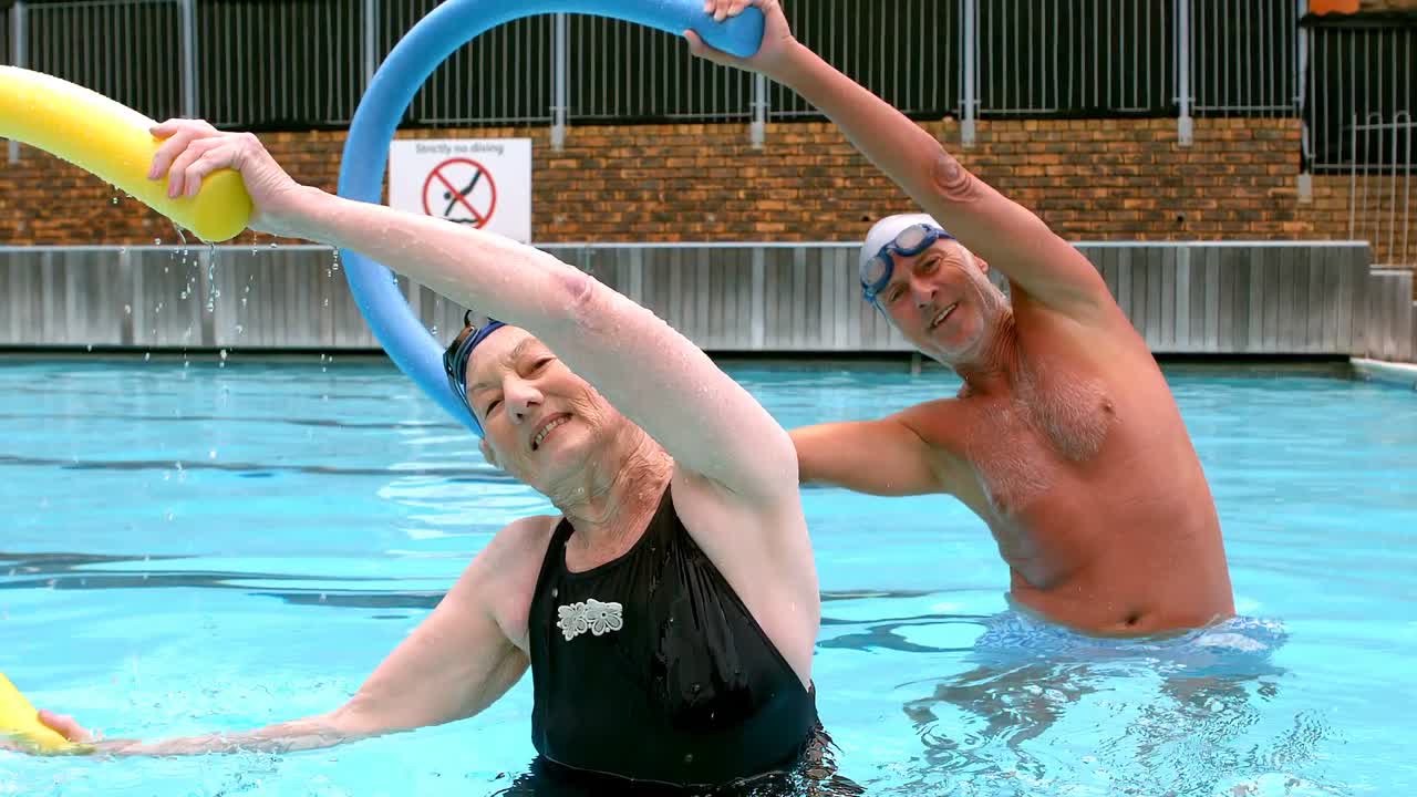 pareja de ancianos haciendo ejercicio con fideos de piscina en la piscina