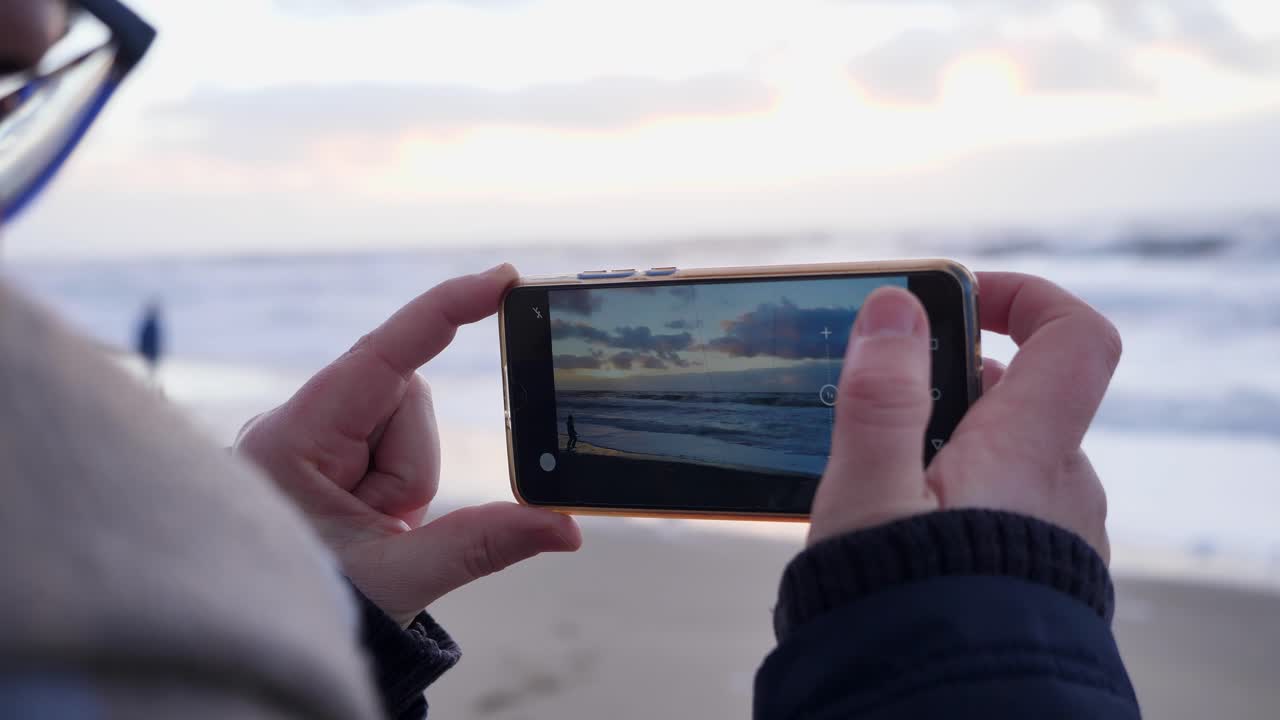 una mujer hace un video con un teléfono inteligente durante la puesta de sol en una increíble playa de sylt