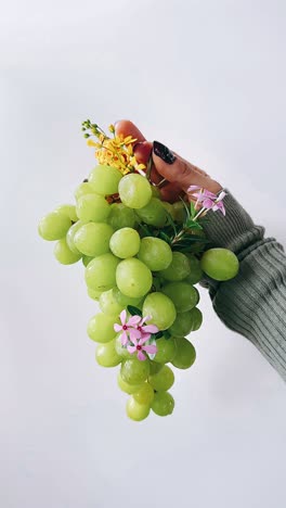 hand holding a bunch of green grapes with flowers