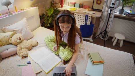 teenage girl studying on a bed with a laptop