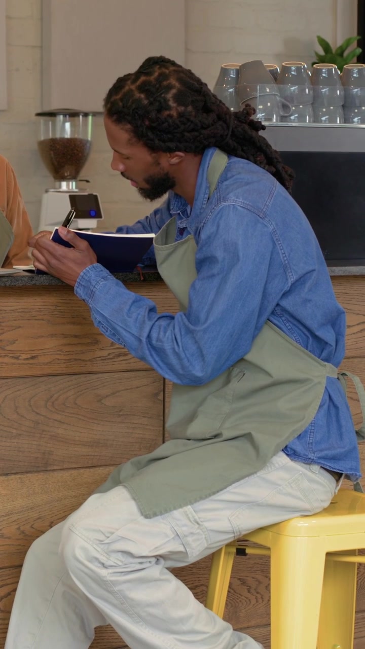 Vertical video: Stirring blue bowl, barista in apron tasting sample at cafe counter, holding spoon