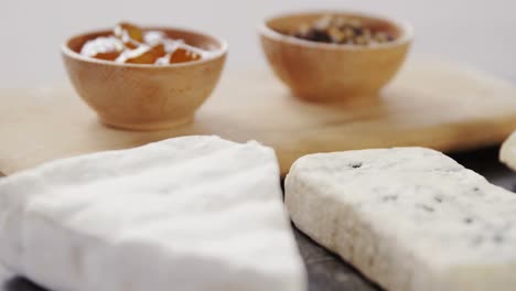 Sliced-cheese,-bowls-of-jam-and-spices-on-wooden-board