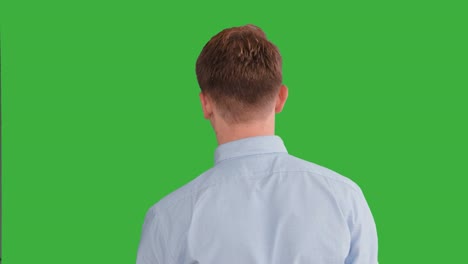 초록색 스크린 앞에서 연기하는 젊은 잘생긴 남성, 금발, 파란 셔츠, 파란 바지, 춤추고, 생각하고, 돌아서서 카메라와 대화합니다.