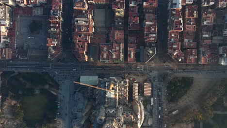 Birds-eye-of-basilica-Sagrada-Familia-and-surrounding-buildings-lit-by-bright-low-sun-at-golden-hour.-Barcelona,-Spain