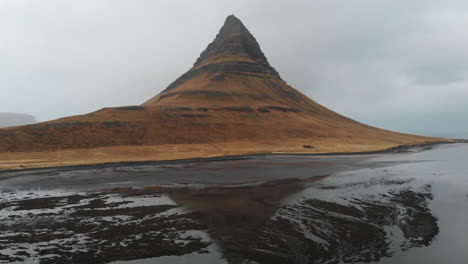 aerial view, highlands of iceland, glacial river in black lava field, volcanic peak and cloudy weather, drone shot