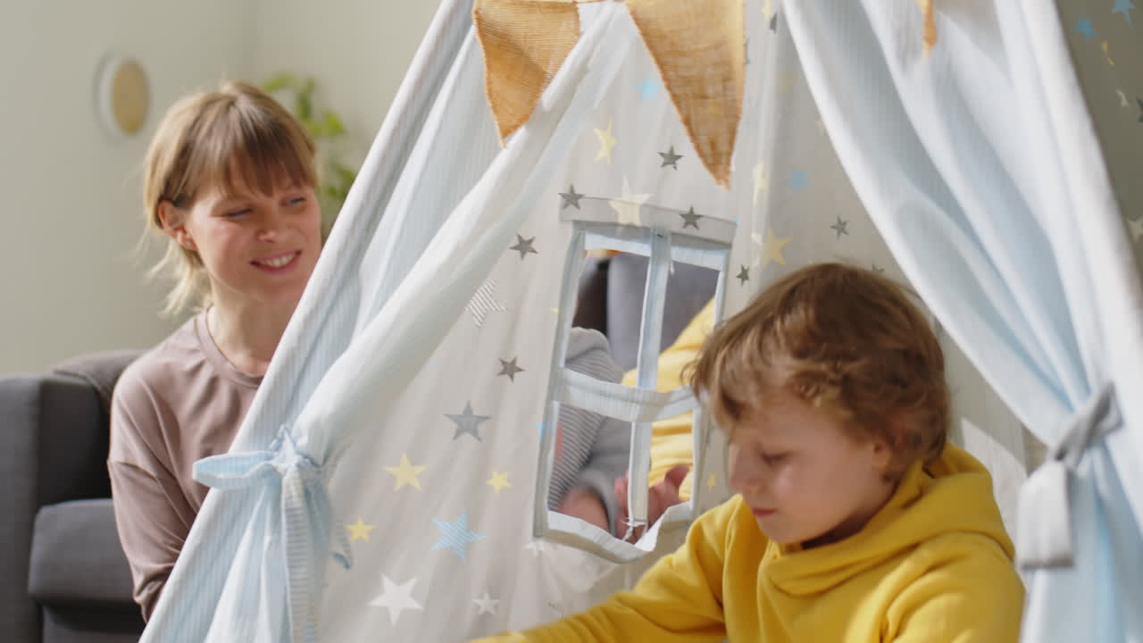 Boy Sitting in Teepee and Playing with Mom and Brother