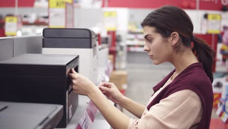 Kundin-Wählt-Neuen-Drucker-In-Der-Elektronikabteilung-Im-Haushaltsgerätegeschäft.-Ich-Komme-Zu-Einer-Vitrine-Und-Betrachte-Sie-Sorgfältig.-Auf-Der-Suche-Nach-Haushaltselektronik.