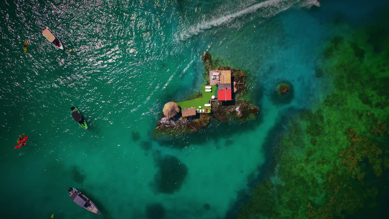 A slow, spinning bird's eye view of this beautiful private bar located on an island in the ocean on the coast of Colombia. A boat is also speeding by at the perfect time!