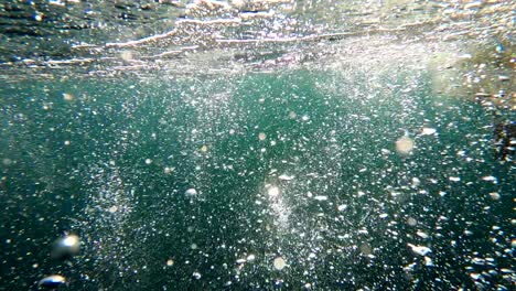 las burbujas cinematográficas se elevan a través del agua del océano abierto, verde y azul.