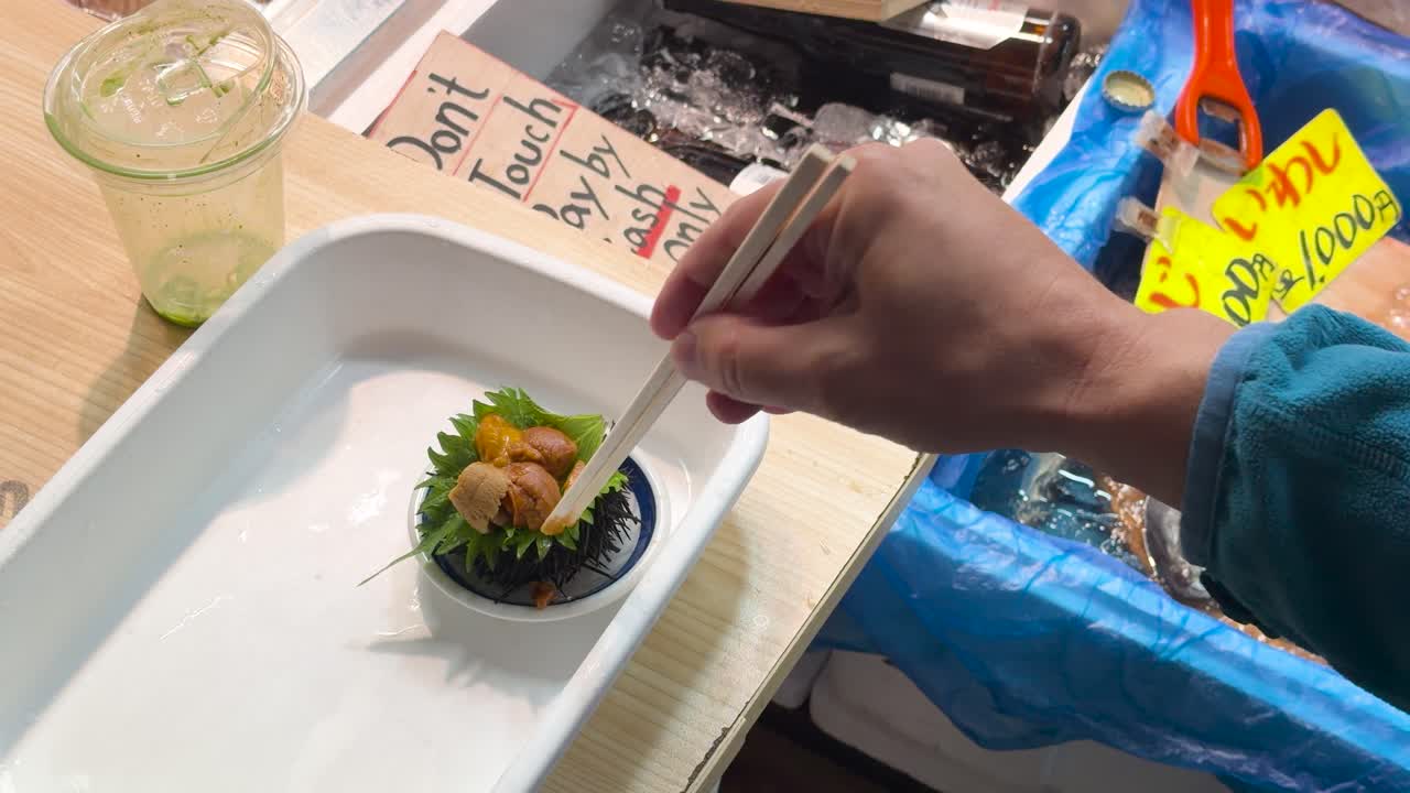 Close-up shot of a hand using chopsticks to eat fresh uni at a Tokyo market