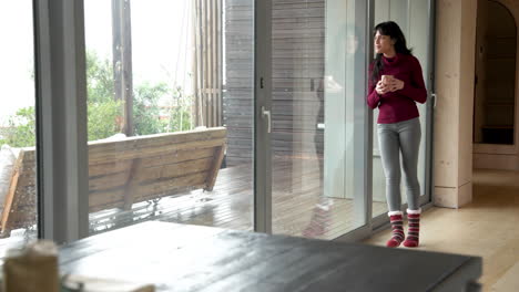 woman enjoying hot drink by window, wearing cozy socks at home, copy space