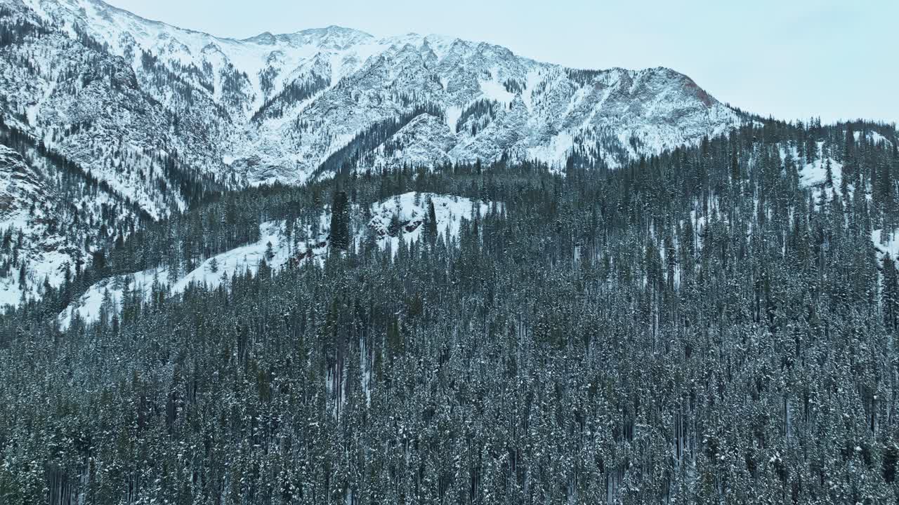 Aerial establishing approach to snow covered mountains and dense evergreen forests in winter, rugged peaks and icy slopes create a dramatic winter landscape