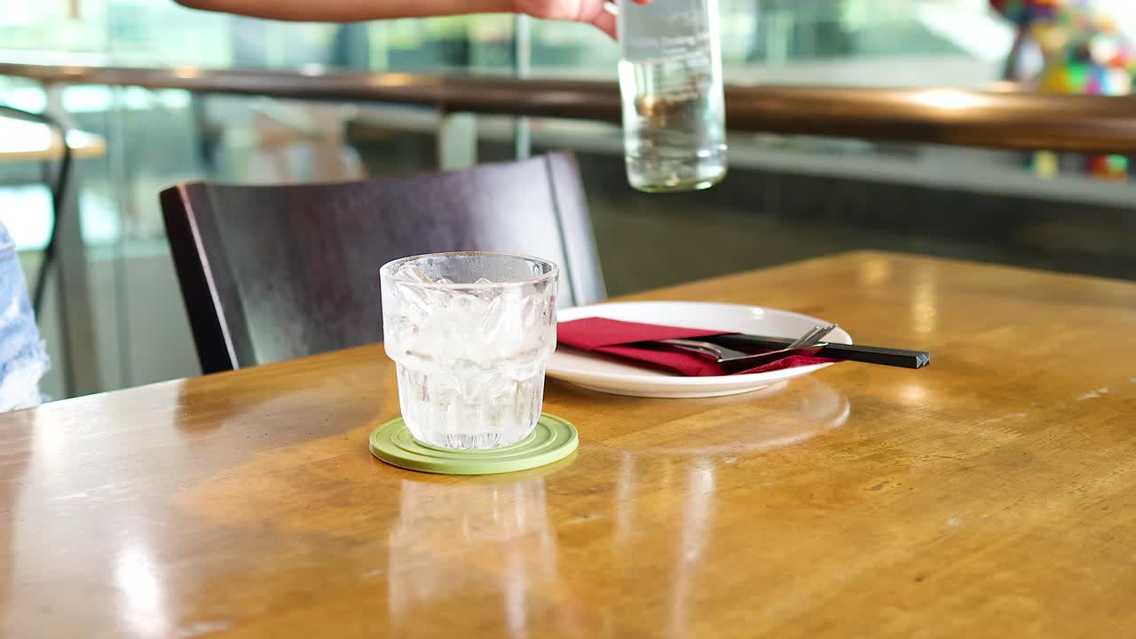 A person pours water into a glass at a restaurant table in Bangkok, Thailand. Bright lighting and casual setting