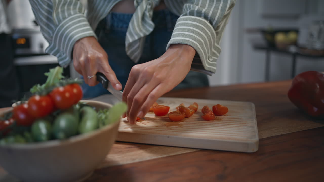Hands cutting cherry tomatoes on kitchen board. Woman preparing healthy salad