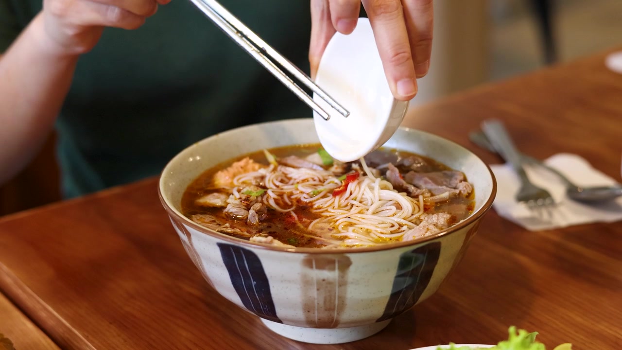 Một cảnh cận cho thấy đôi tay thêm ớt đỏ vào bún chả Việt Nam bằng đũa.